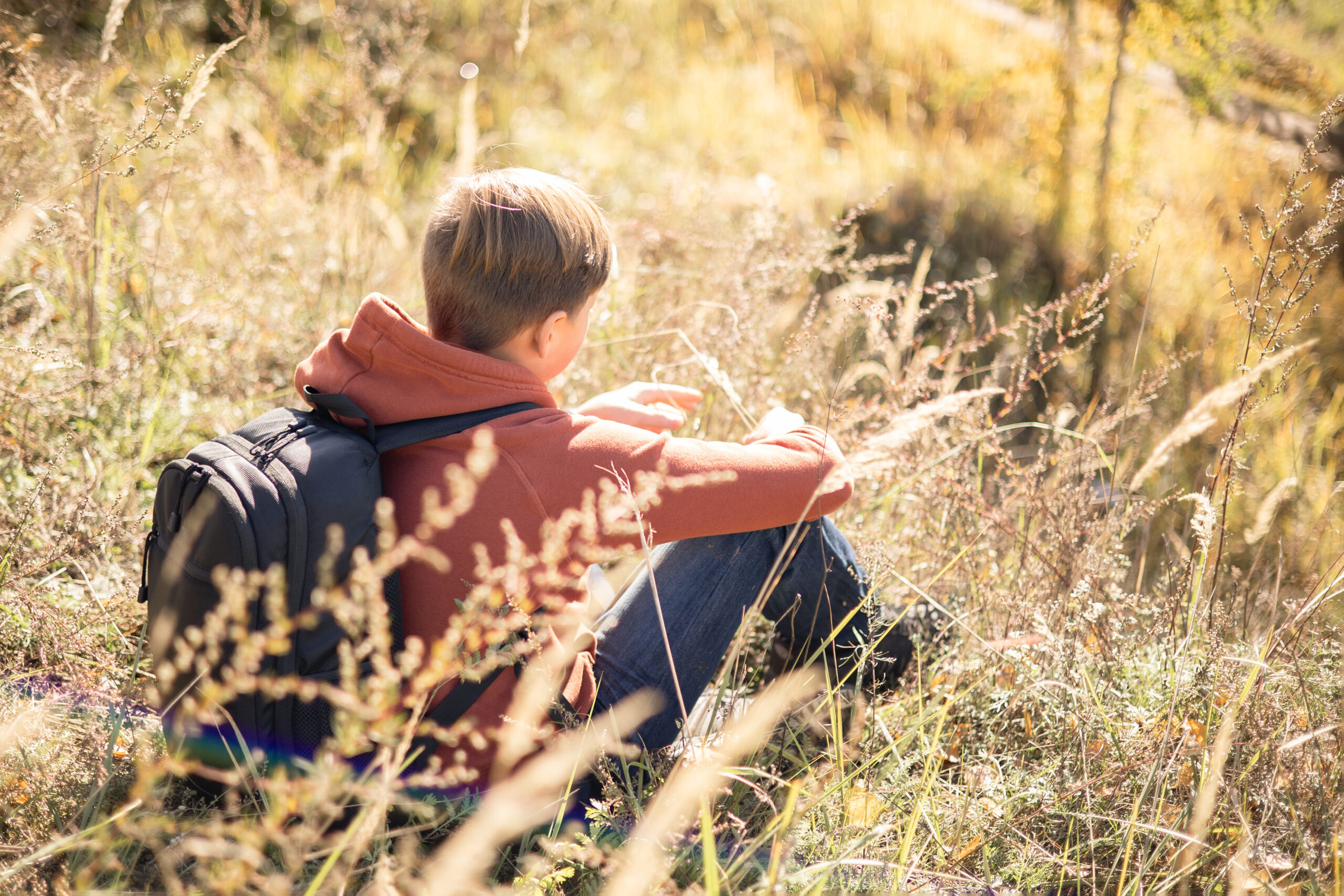 Autumn portrait of teenager boy sitting on grass. Young man with backpack resting relaxing, contemplating, thinking, daydreaming. Teen deep in thought Local travel. Active lifestyle People from behind Autumn portrait of teenager boy sitting on grass. Young man with backpack resting relaxing, contemplating, thinking, daydreaming. Teen deep in thought Local travel. Active lifestyle People from behind